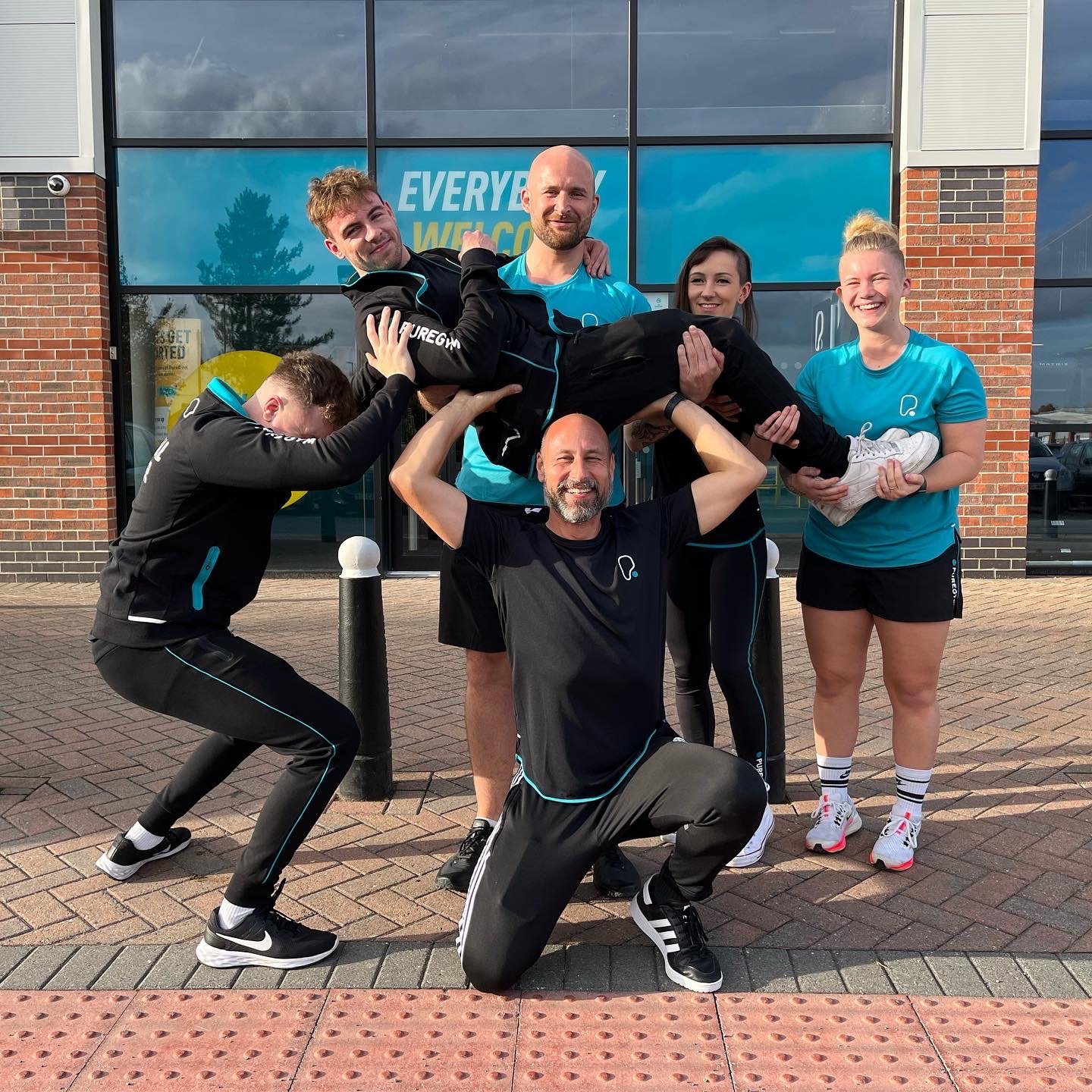 Team pose outside a gym; people holding a person up.
