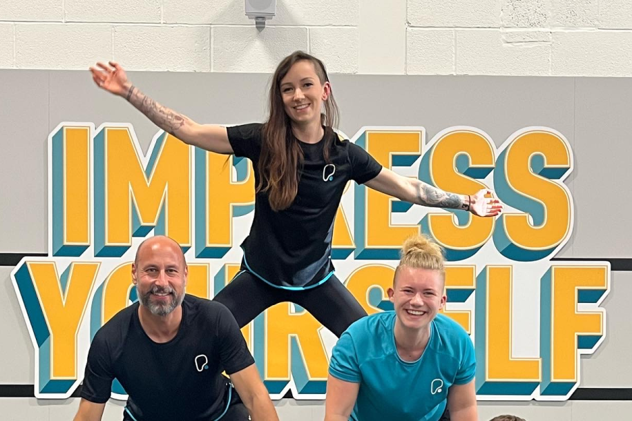 Six gym staff members in branded activewear posing in a human pyramid formation.