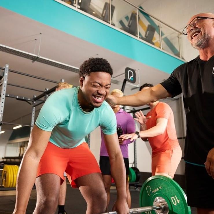 A personal trainer cheering on a young man as he lifts a heavy barbell during a gym workout.