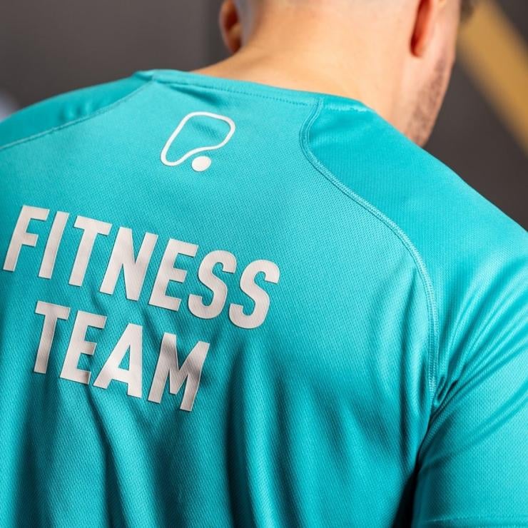A close-up view of a person wearing a turquoise athletic shirt with the text FITNESS TEAM printed.